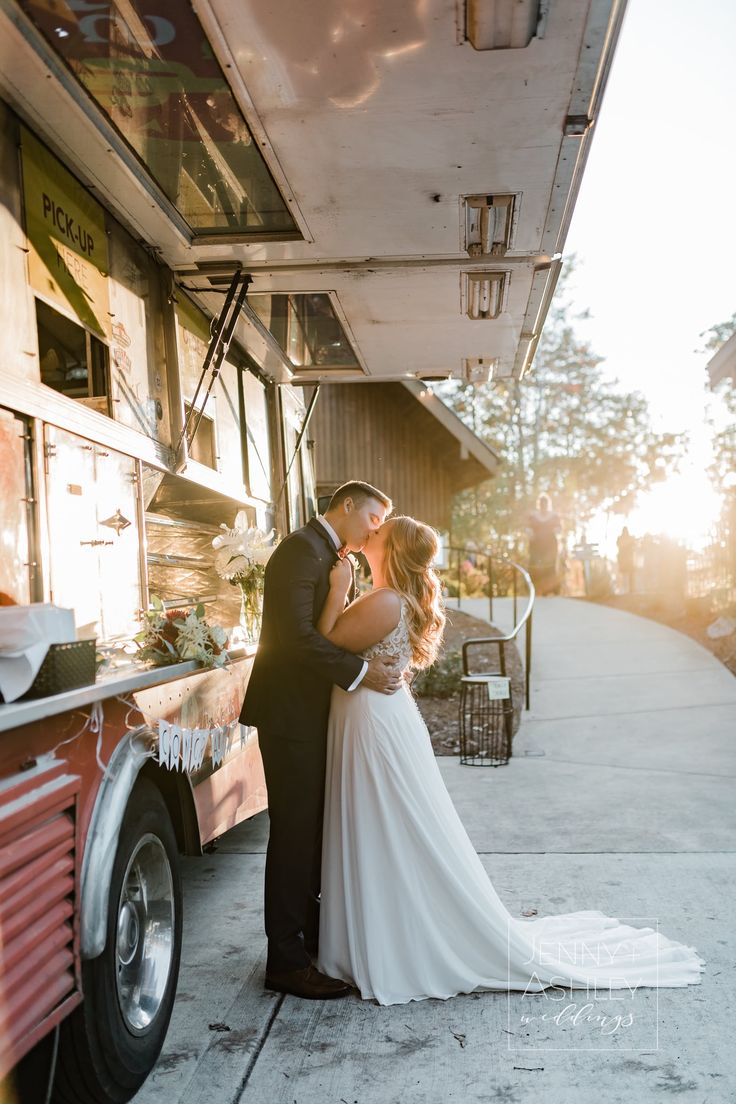 a bride and groom kissing in front of a food truck on the sidewalk at sunset