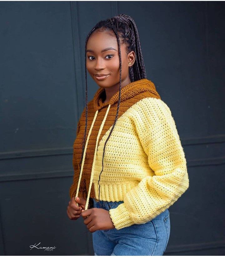 a woman with braids standing in front of a black door wearing a yellow sweater