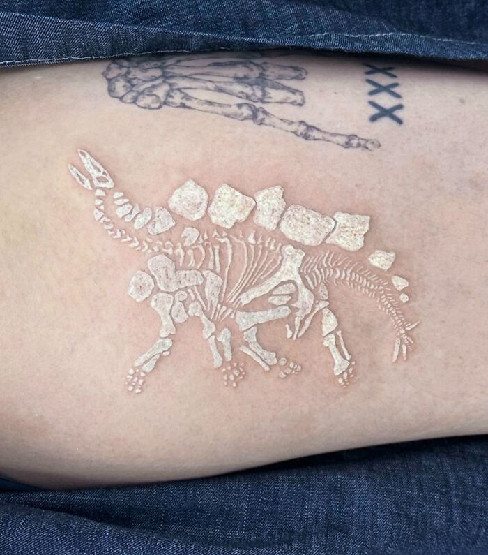 a person with a tattoo on their arm and the skeleton of a dinosaur behind it