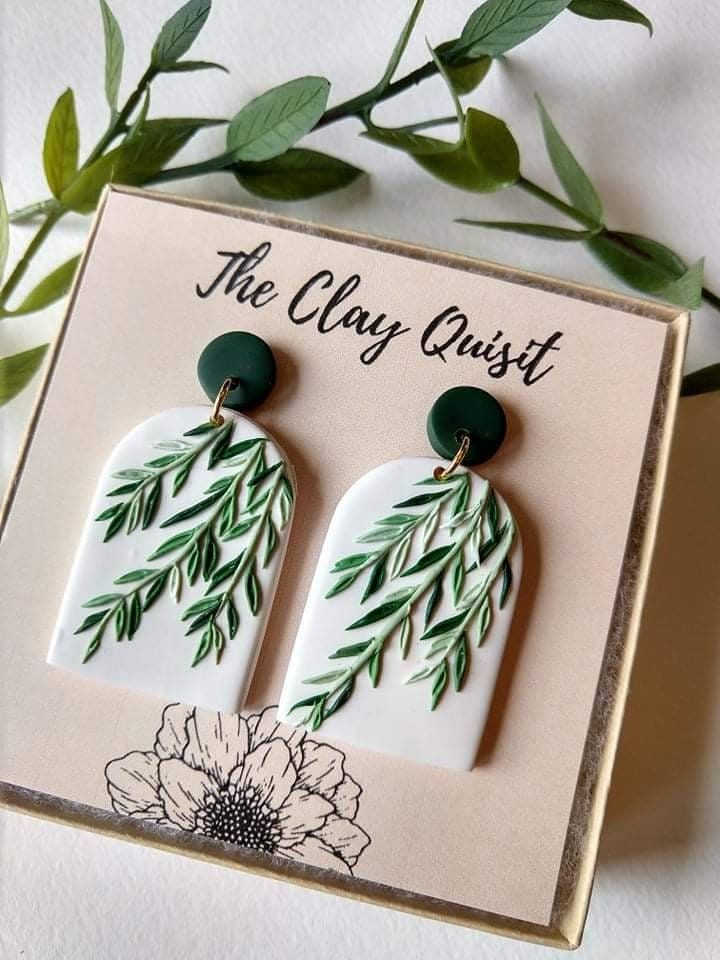 a pair of earrings with green leaves and flowers on them, sitting on top of a card