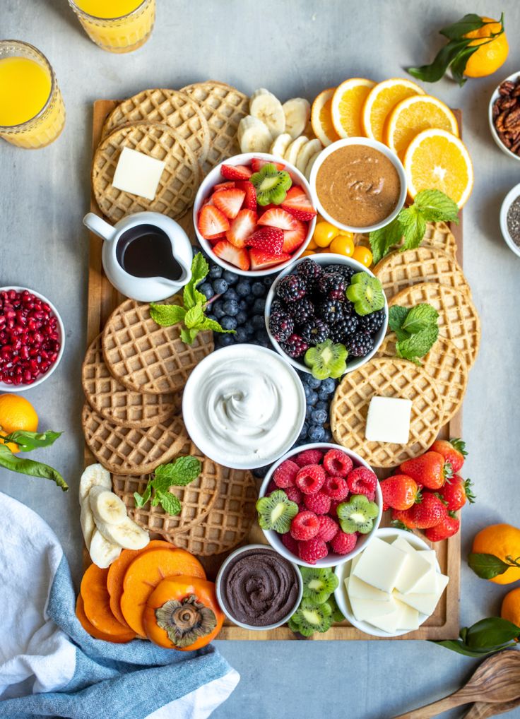 a table topped with waffles covered in fruit and dips next to oranges