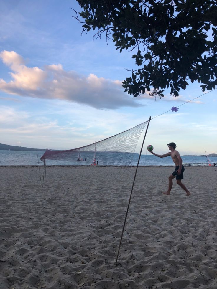 a man playing volleyball on the beach with his net and ball in front of him