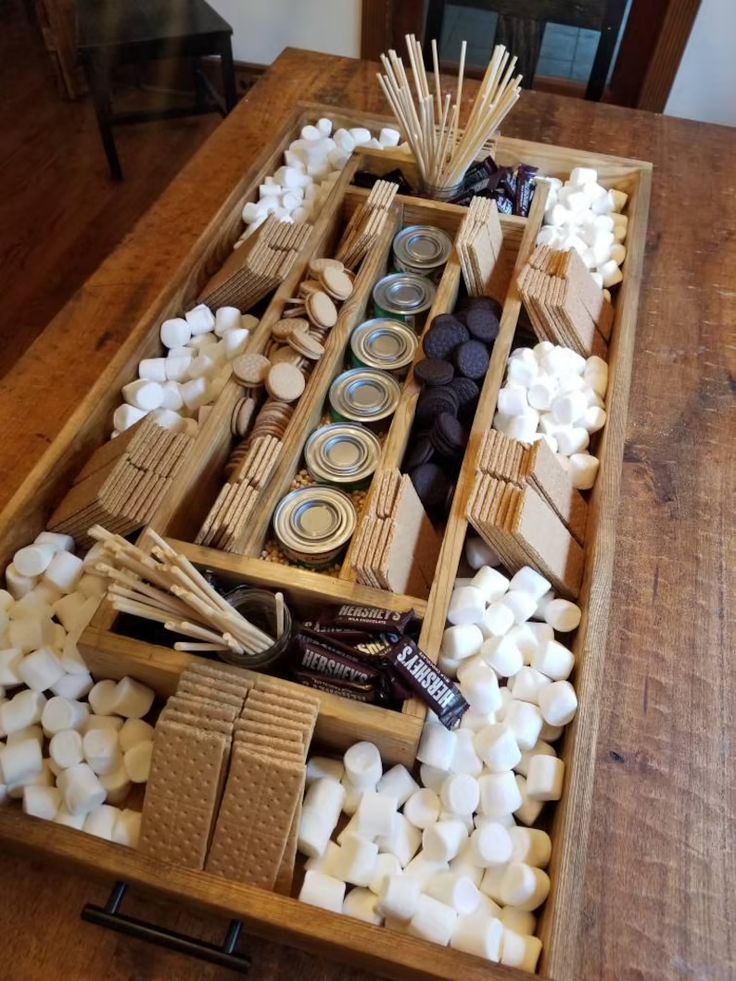 a wooden tray filled with marshmallows and other items on top of a table