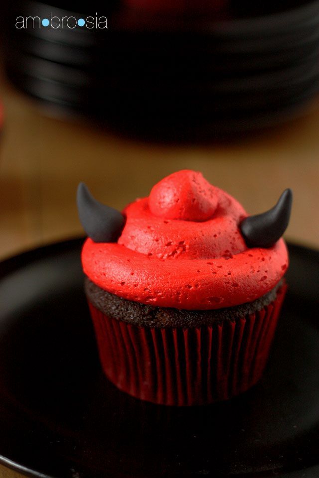 a cupcake with red frosting and black horns on it sitting on a plate