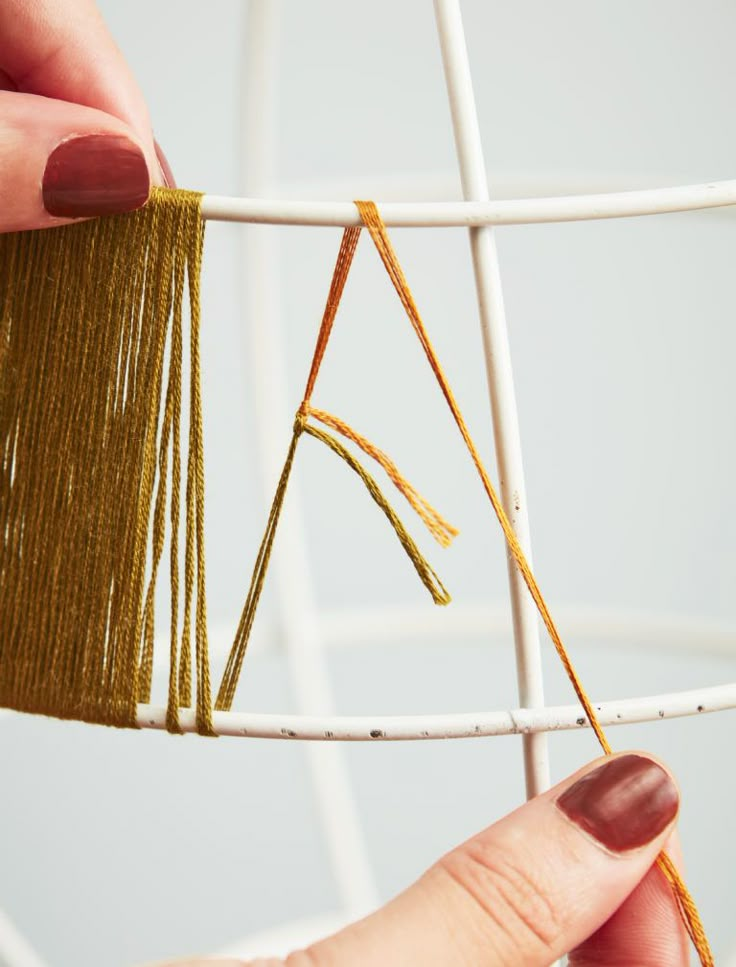 two hands are stitching together string on a piece of white material with gold thread