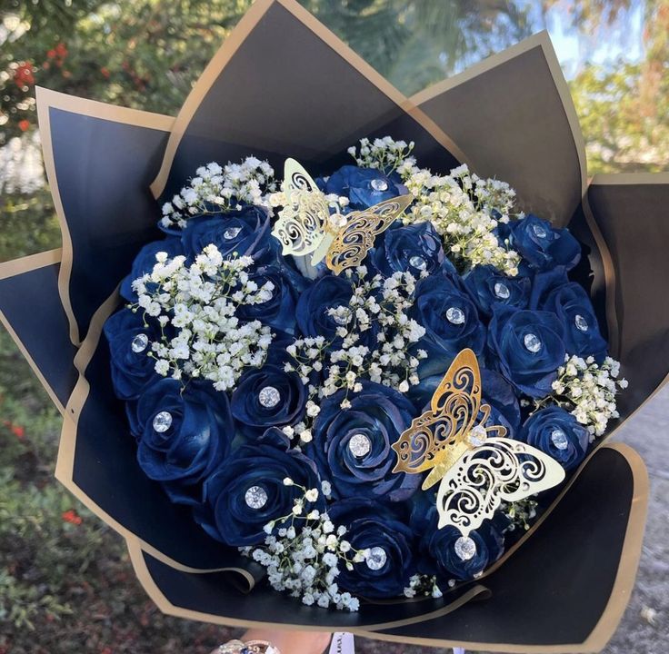 a bouquet of blue roses with butterfly brooches on it in someone's hand