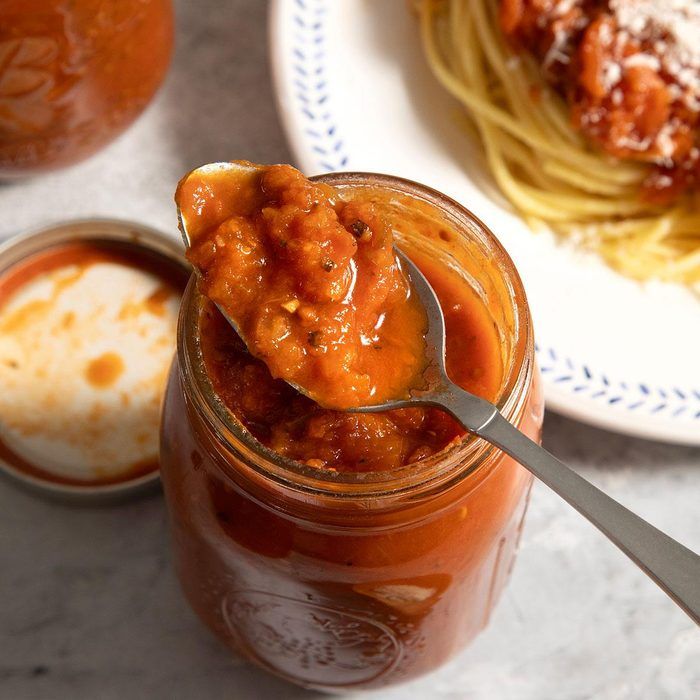 a spoon full of sauce sitting on top of a table next to pasta and spaghetti