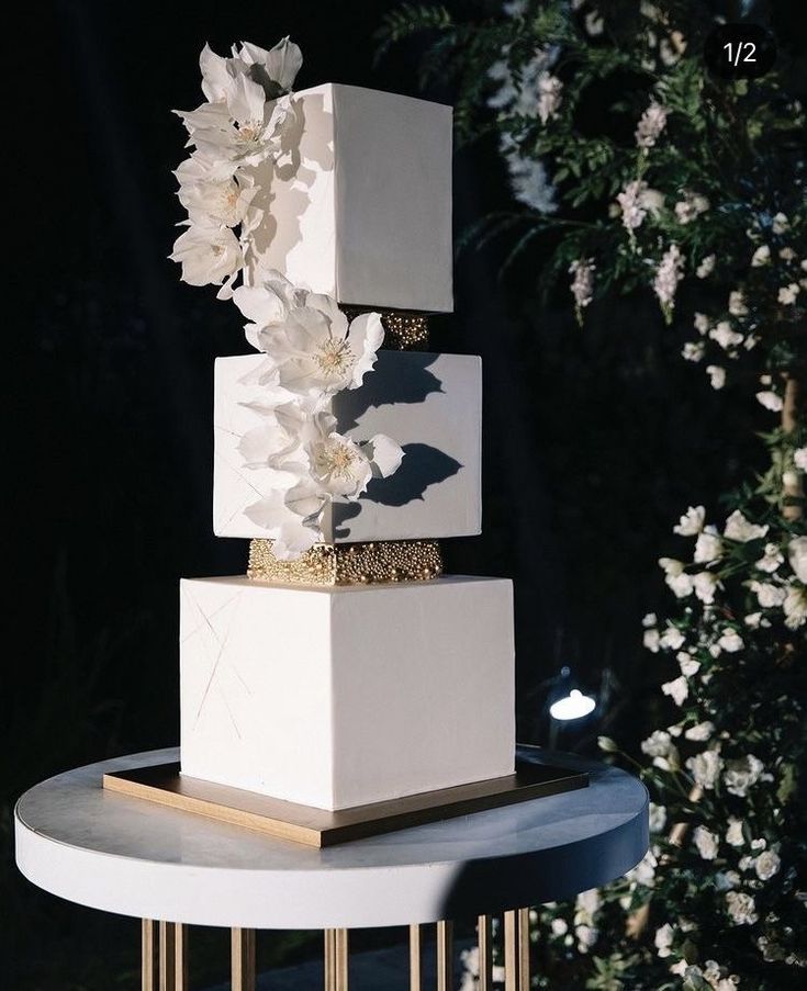 a three - tiered cake with white flowers on top and gold trimmings