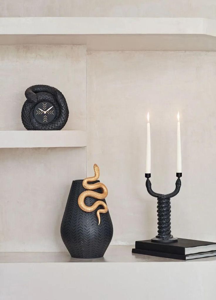 a black vase sitting on top of a white shelf next to a lit candle holder