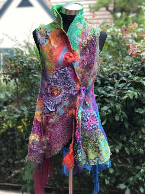 a woman's colorful vest on display in front of bushes