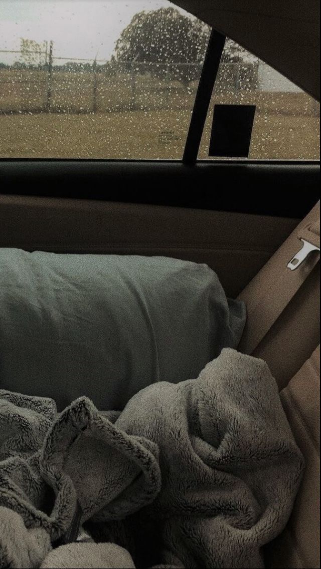 a blanket and pillows in the back seat of a car with rain coming down on it