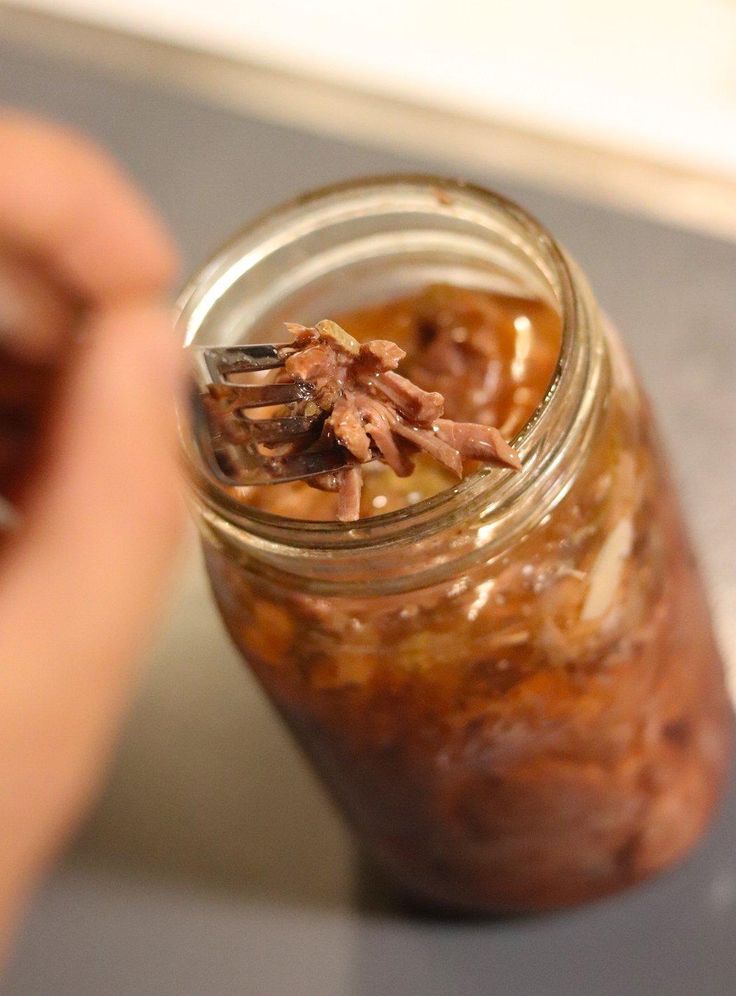 a person holding a spoon in a jar filled with food