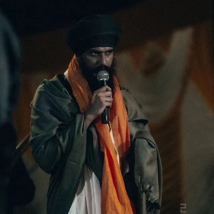 a man with a microphone in his hand and wearing an orange scarf around his neck