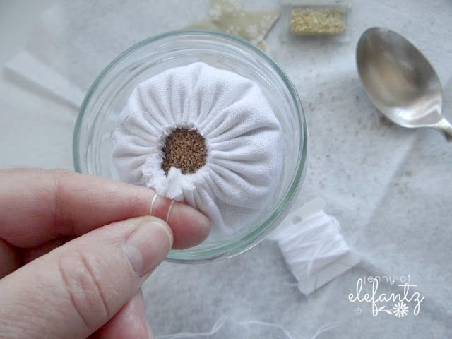 a person holding a tiny flower in a glass bowl with spoons and sugar cubes around it