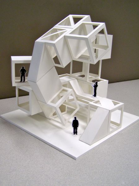 two people standing in front of a model of a building with white walls and floors