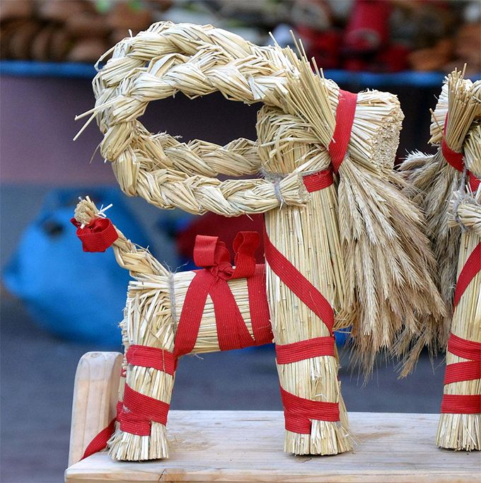 two straw horses are sitting on a wooden stand with red ribbon around their necks and legs