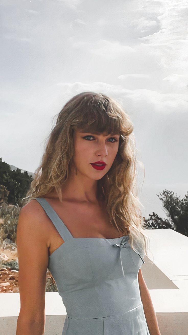 a woman with long hair wearing a gray dress and red lipstick standing in front of a white wall