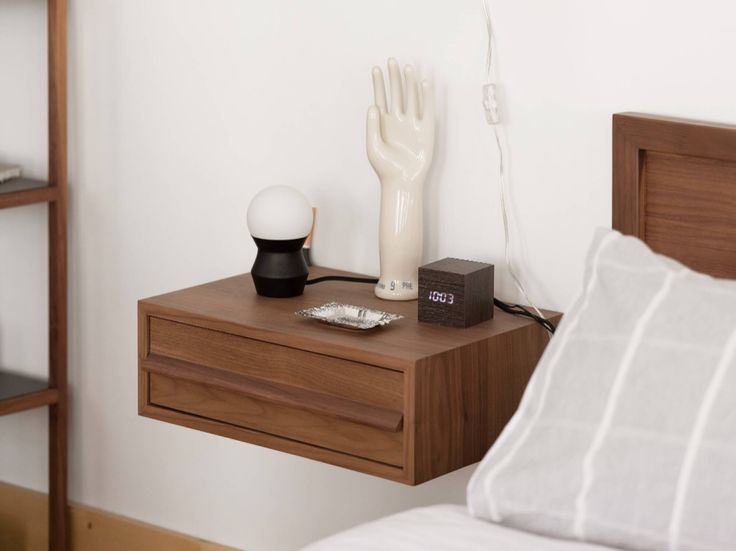 a bedside table with an alarm clock, lamp and hand statue on it next to a bed