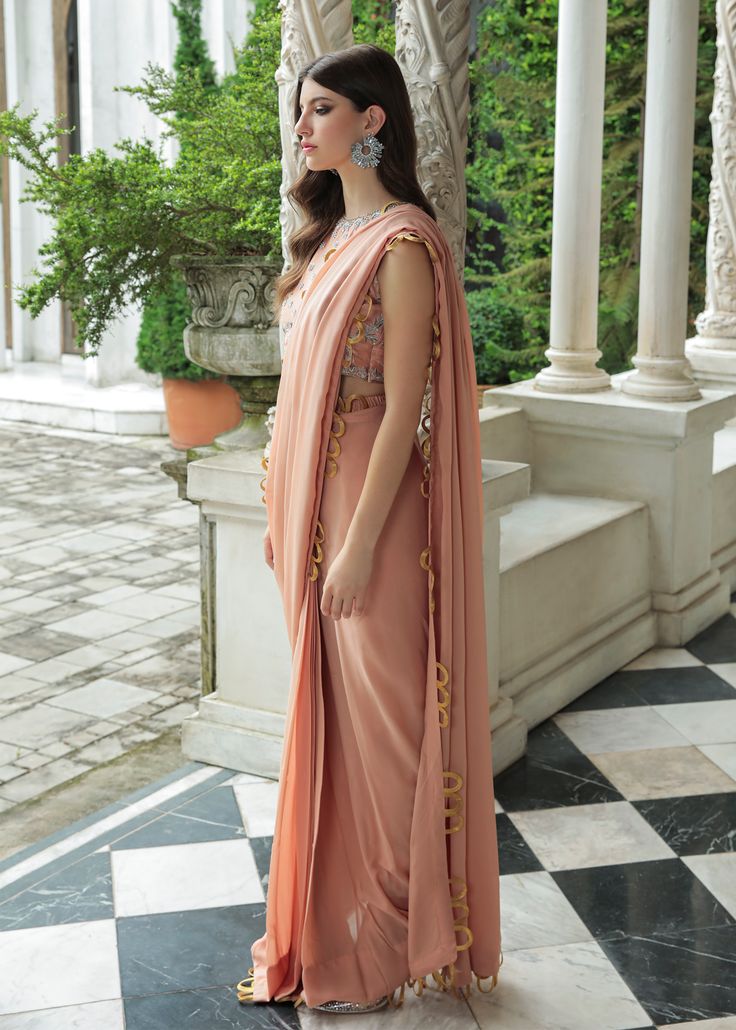 Look bold and elegant in this fusion of Saree Pants adorned with gold loop sets all across the borders. The blouse is fully hand worked with zardozi, tilla, dabka and small saworski crystals. The same work is embodied on the fully worked rawsilk pants. Formal Hand Embellished Pre-draped Saree, Anarkali Style Hand Embellished Pre-draped Saree, Elegant Pre-draped Saree With Gota Work, Traditional Hand Embellished Pre-draped Saree For Diwali, Traditional Hand Embellished Silk Pre-draped Saree, Eid Reception Pre-draped Saree With Gota Work, Gold Silk Palazzo Set With Mirror Work, Gold Anarkali-style Pre-draped Saree Embellished, Gold Embellished Anarkali Pre-draped Saree