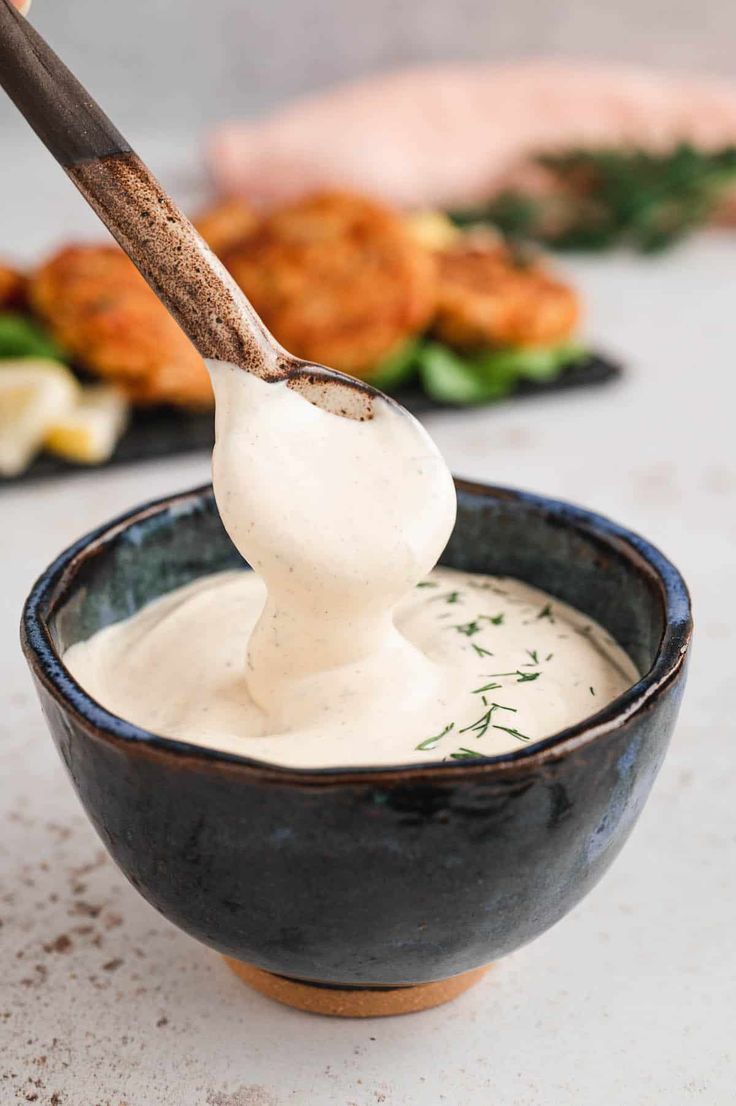 a spoon full of ranch dressing in a black bowl on a white table with other food