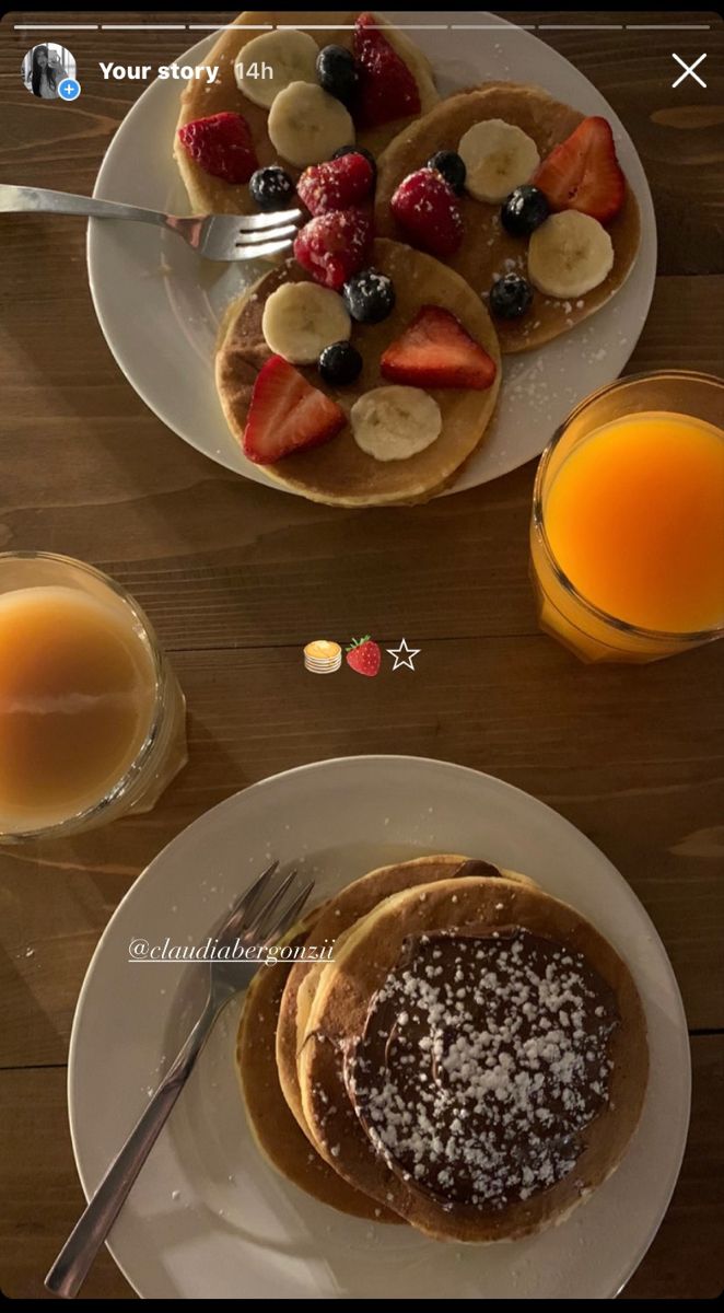 two plates with pancakes and fruit on them next to glasses of orange juice in front of them