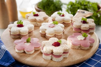 a wooden plate topped with mini sandwiches covered in frosting