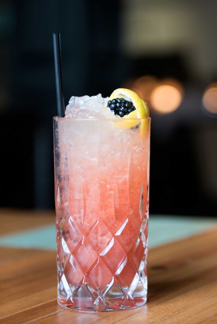 a pink drink with lemon and blackberries on the rim sitting on a wooden table