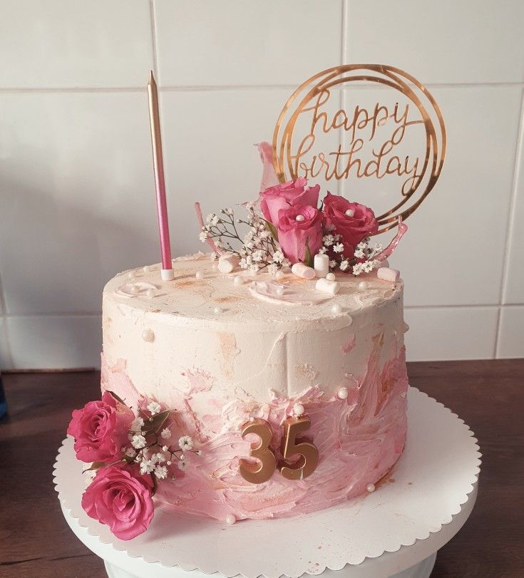 a birthday cake decorated with pink flowers and a gold happy birthday sign on the top