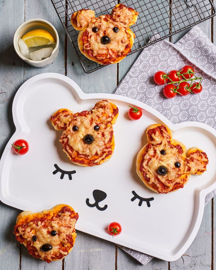 mini pizzas shaped like bears with toppings on a white platter next to a cooling rack