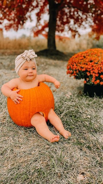 a baby sitting on the ground wearing an orange knitted pumpkin costume with her legs crossed