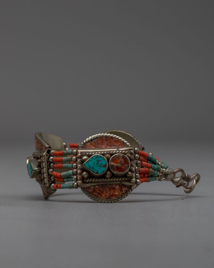 an old silver bracelet with turquoise and red beads on the clasp, sitting against a gray background