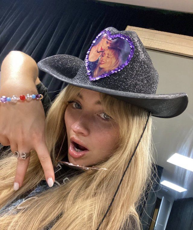 a woman wearing a black hat with a purple heart on it's brim