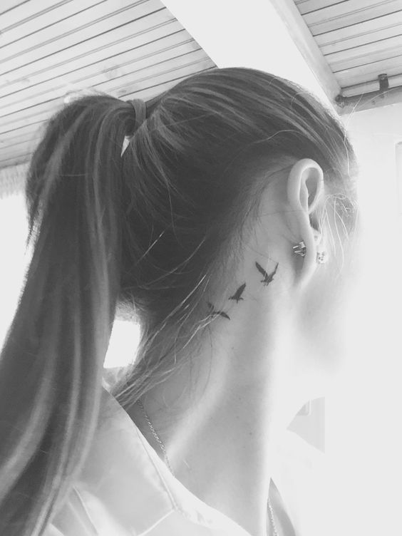 a woman with a bird tattoo on her left side behind her ear is looking out the window