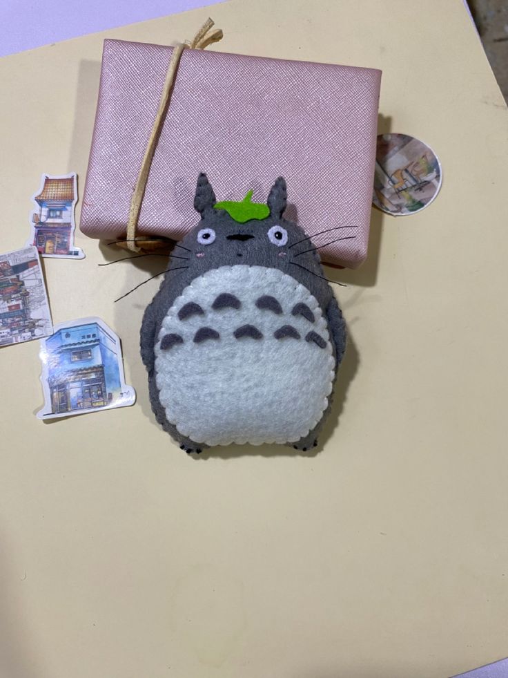 a totoro stuffed animal sitting next to a pink gift bag on top of a table