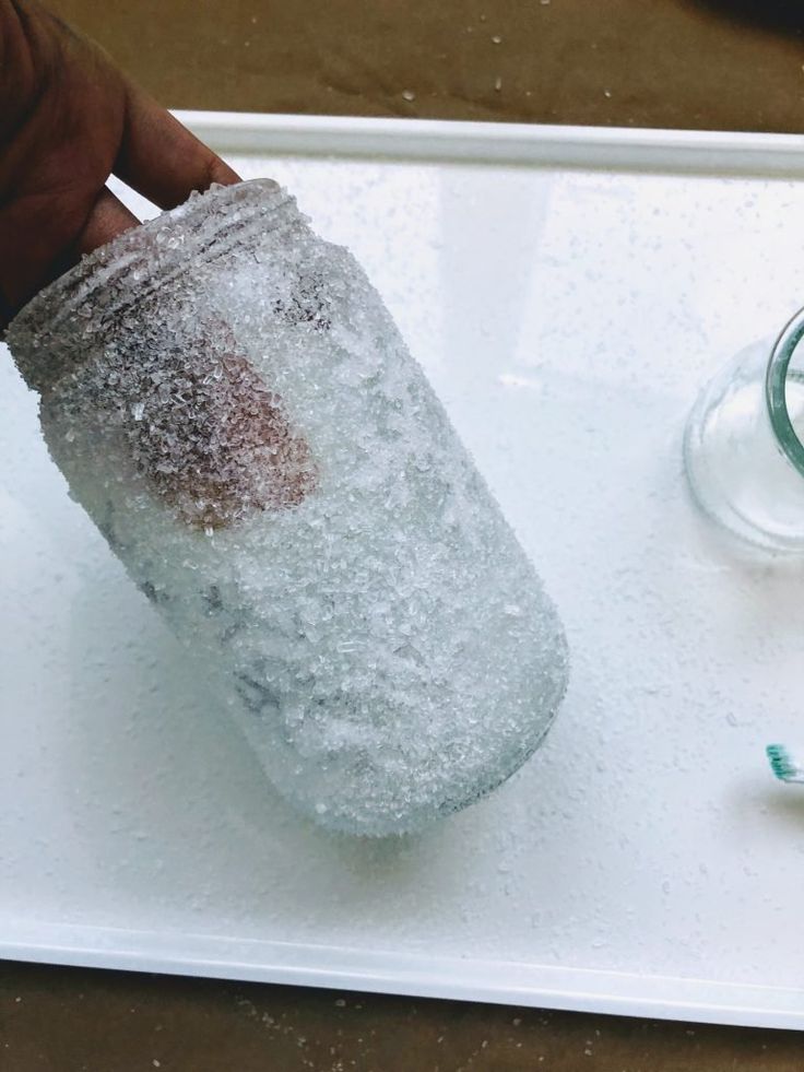 a person is holding a glass with some ice on it and toothbrushes next to it