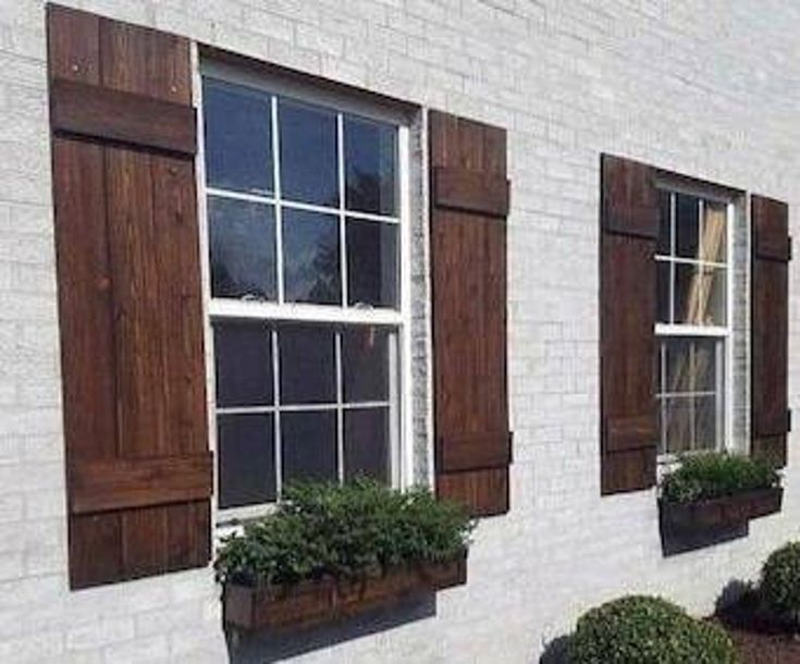 three windows with wooden shutters on the side of a white brick building, and two planters in front of them