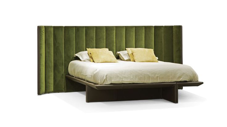 a bed with green velvet headboard and yellow pillows on the top, sitting in front of a white backdrop