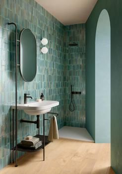 a bathroom with green tile and wood flooring next to a white sink under a mirror