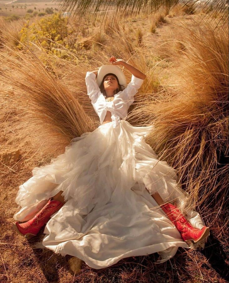 a woman in a white dress and hat laying on the ground