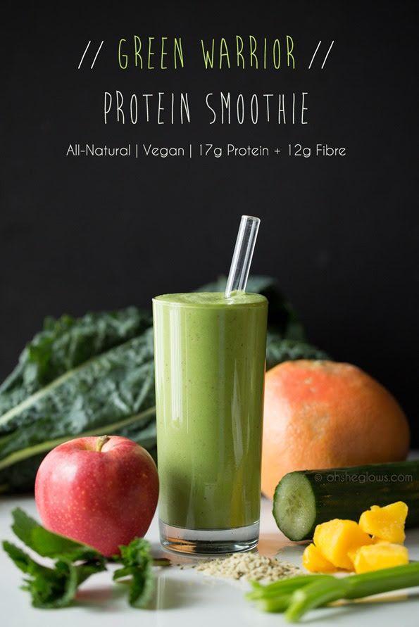 a green smoothie in a glass surrounded by fruits and vegetables on a white table