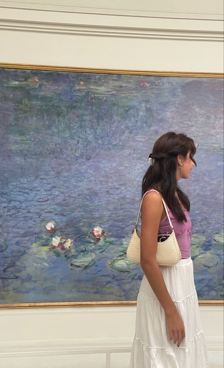 a woman standing in front of a painting with water lillies on it's wall