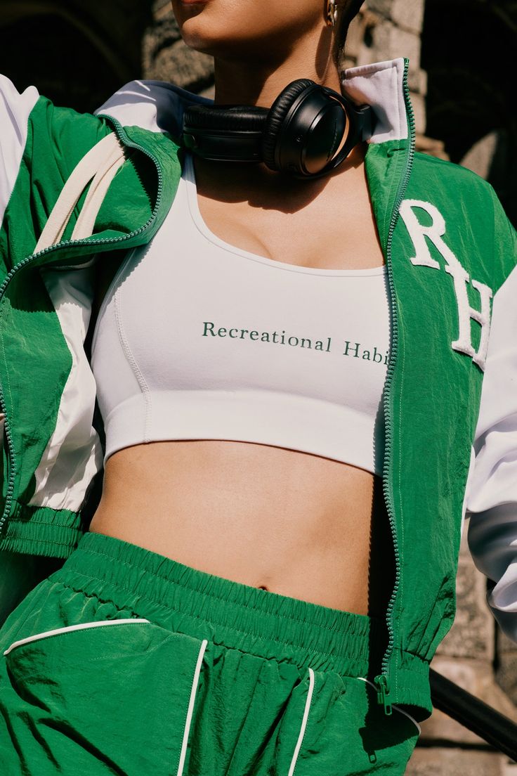 a woman with headphones on wearing green sweatpants and a white cropped top