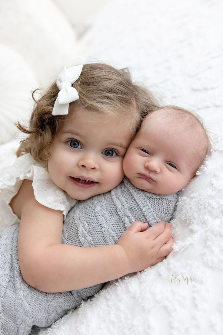 two baby girls cuddle together on a white blanket