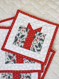 two red and white quilted placemats with holly designs on them sitting on a bed