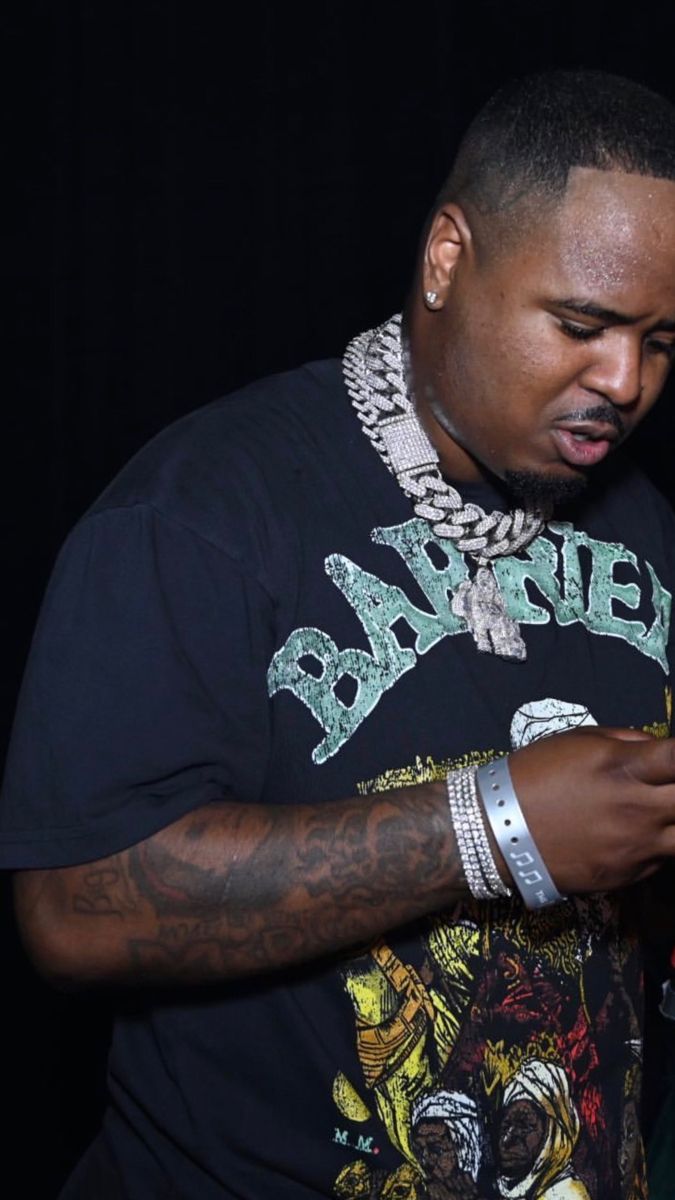 a man in a black shirt is looking at his cell phone while wearing a chain around his neck