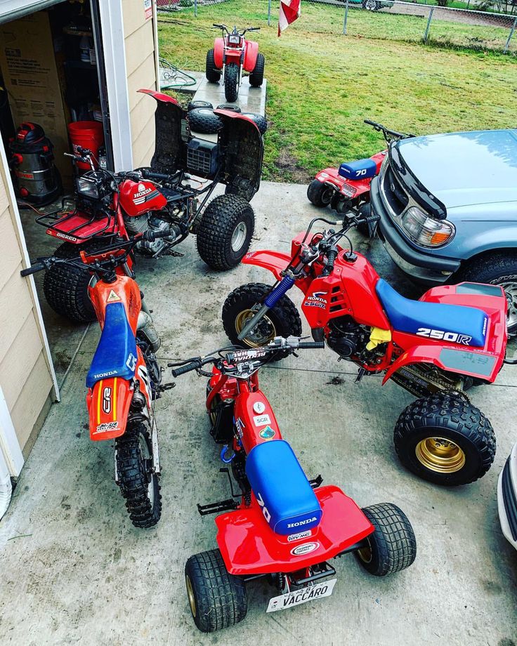 four red and blue atvs parked in front of a garage with two cars behind them