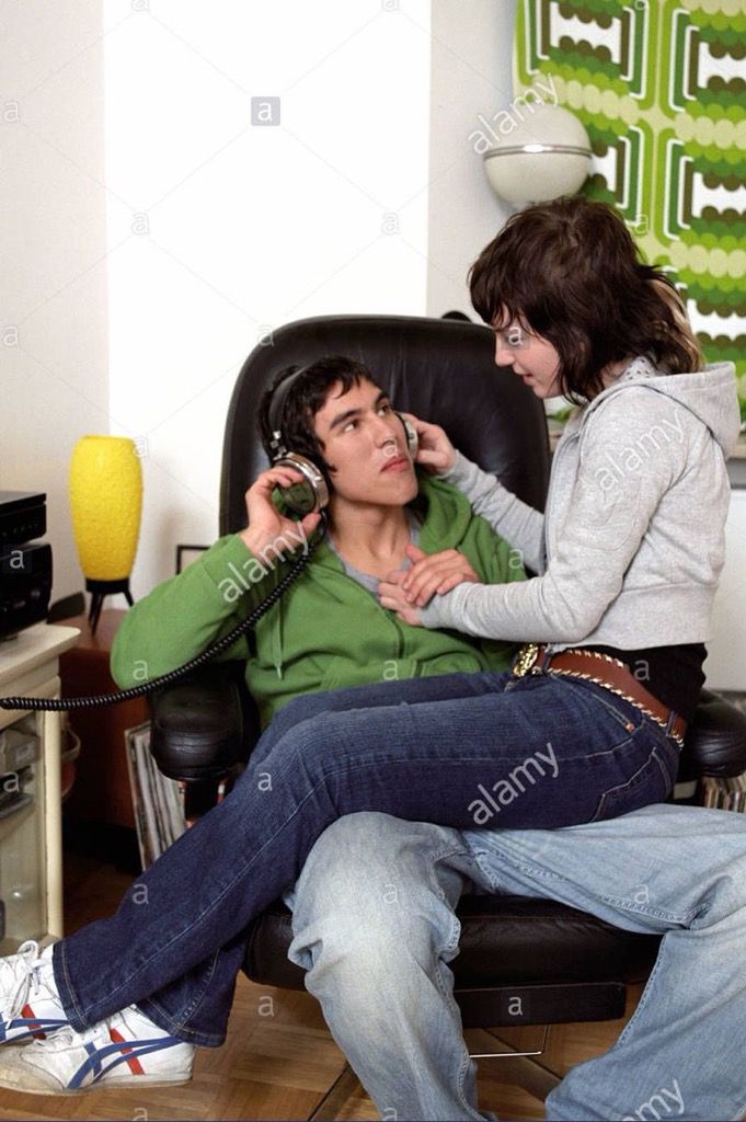 a woman sitting in a chair talking on the phone to a man who is listening to music