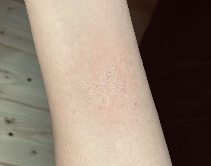 a small white butterfly tattoo on the arm