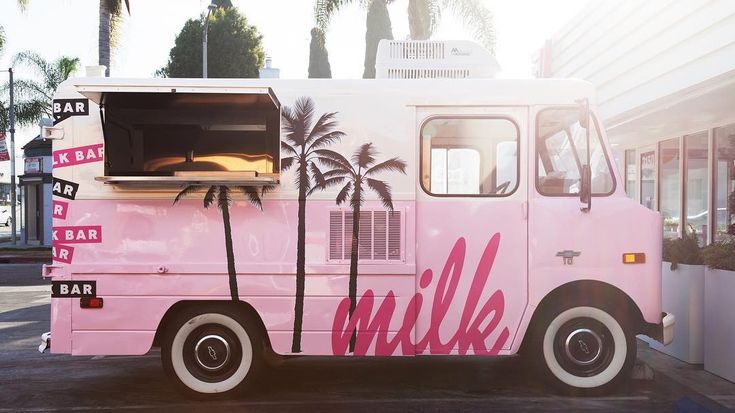 a pink milk truck parked in front of a building with palm trees on the side