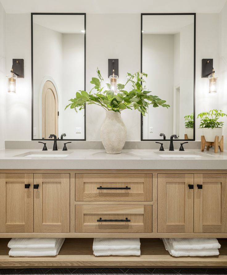 a bathroom with two sinks, mirrors and plants in the vase on the counter top